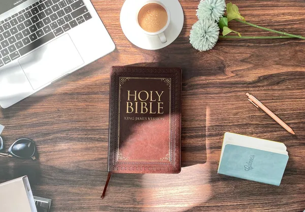 A Bible, laptop and notebook on a wooden desk